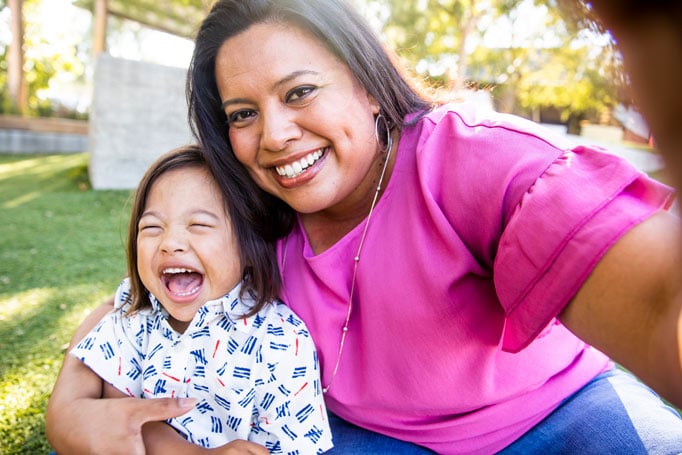 Woman in pink shirt holding her child, who is laughing