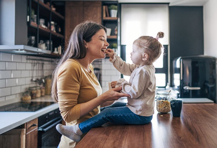 Daughter sitting on kitchen counter feeding her mother a snack