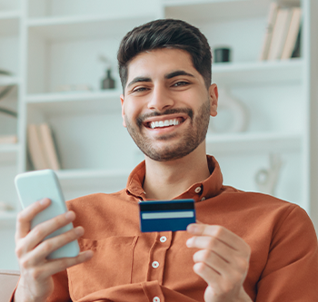 man smiling and holding a credit card and phone