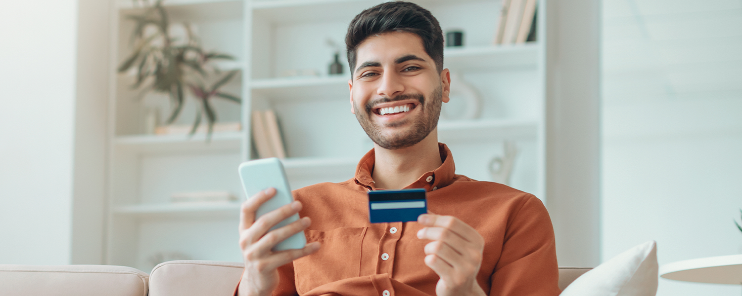 man smiling and holding a credit card and phone