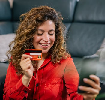 Person sitting on the floor in a living room, holding a credit card and using a smartphone to complete an online purchase.
