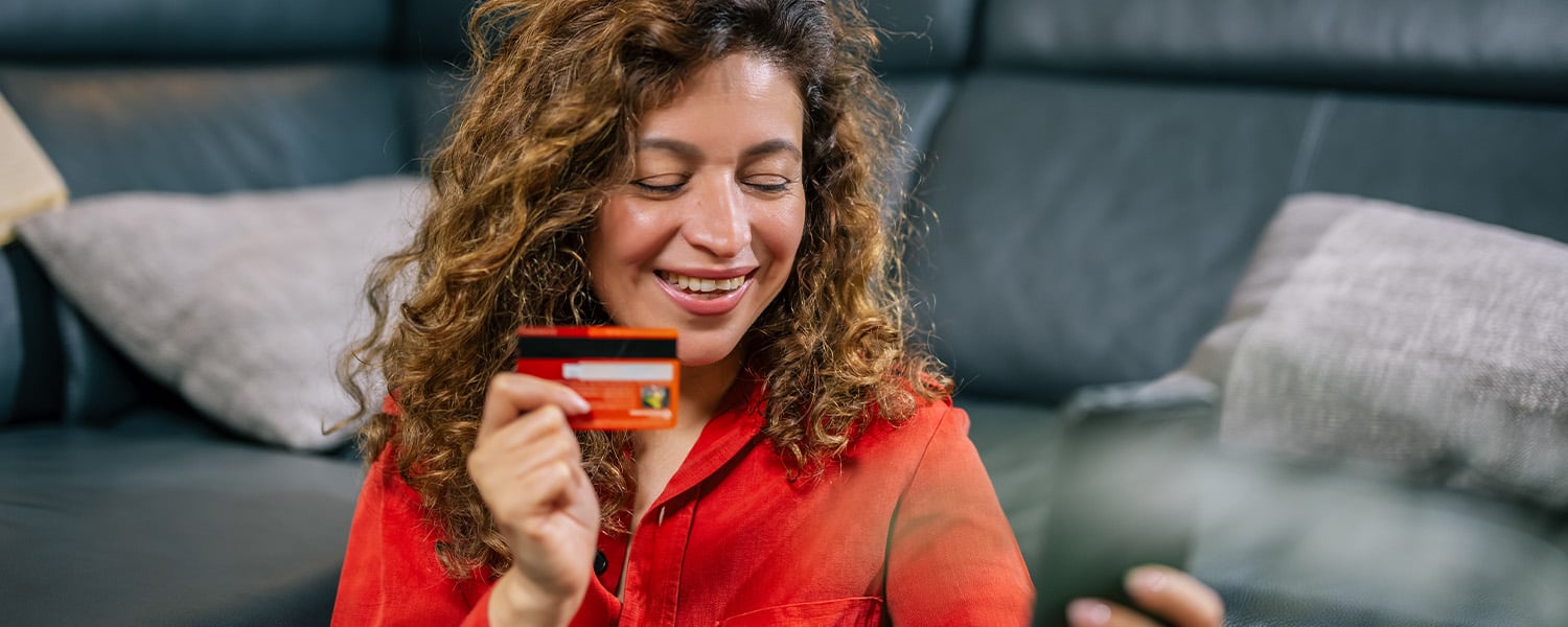 Person sitting on the floor in a living room, holding a credit card and using a smartphone to complete an online purchase.