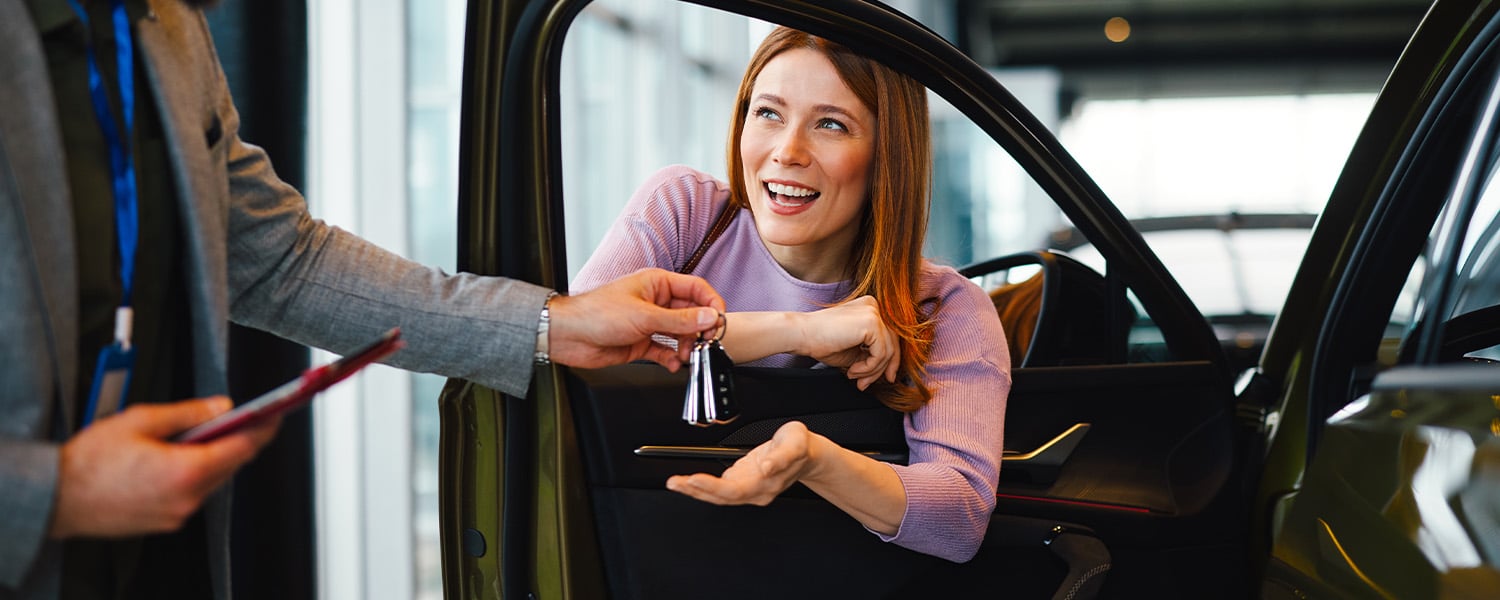 Customer receiving car keys from a dealership representative while seated in a newly purchased vehicle.