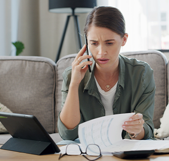 Woman looking stressed while on the phone looking at her finances.