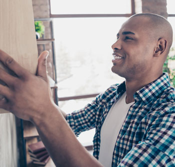 Man in blue plaid hanging a shelf on the wall