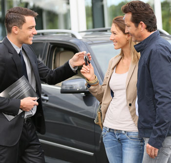 Car salesman handing keys to a couple that just purchased a new car