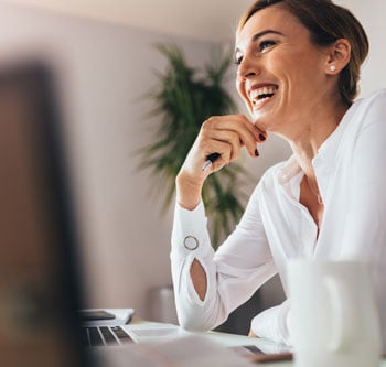 Woman in white shirt sitting at her desk and laughing