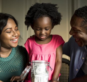 Young girl surrounded by her parents and looking at a jar filled with dollar bills