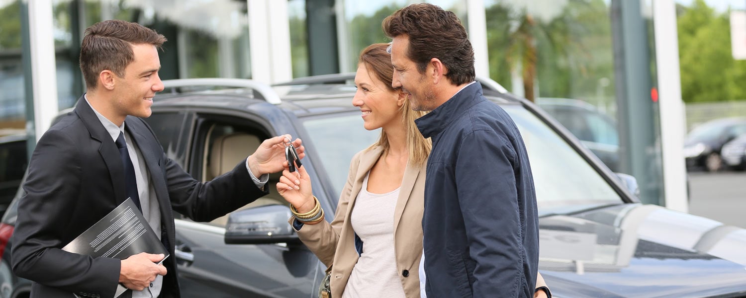 Car salesman handing keys to a couple that just purchased a new car