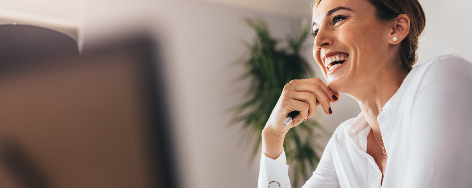 Woman in white shirt sitting at her desk and laughing