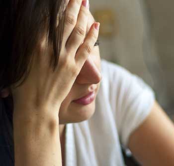 Close up of woman in white shirt holding her head up and looking upset