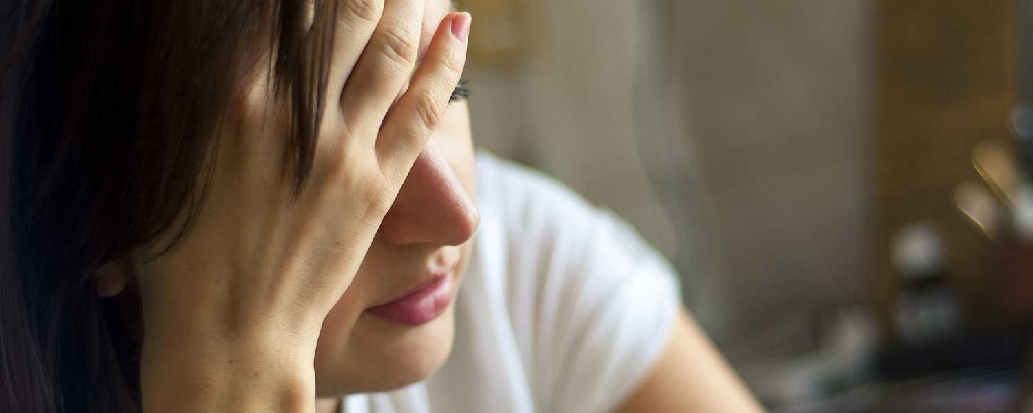 Close up of woman in white shirt holding her head up and looking upset