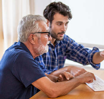 Son helping his elder father on a computer.