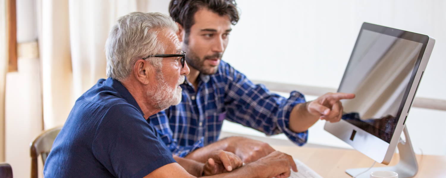 Son helping his elder father on a computer.