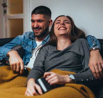 Couple sitting on the couch under a blanket, laughing together