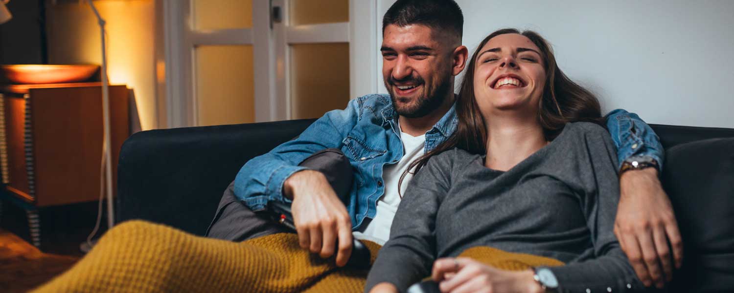 Couple sitting on the couch under a blanket, laughing together