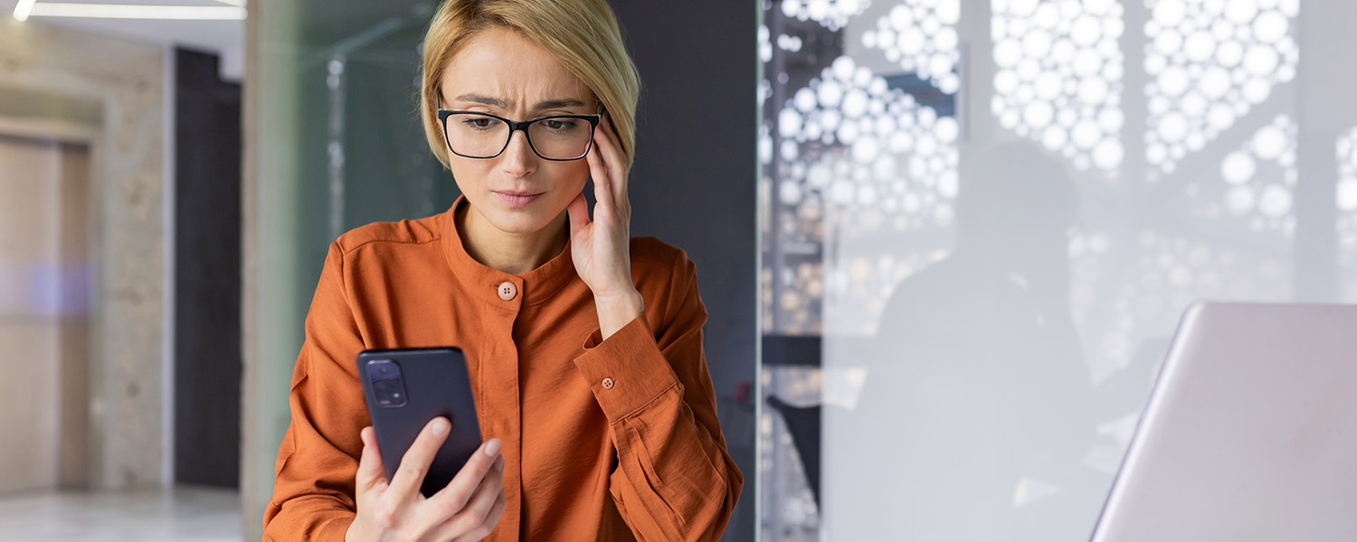 Woman in an orange shirt looking stressed out while staring at her phone