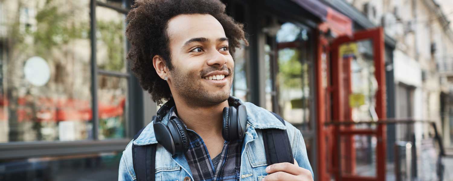 Man in a jean jacket and headphones walking down the street