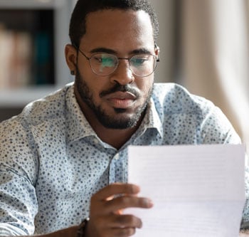 Man in glasses staring pensively at a piece of paper