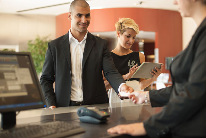 Man handing credit card to woman behind counter while another woman looks at a tablet