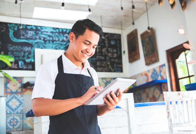 Store employee wearing an apron and smiling down at his tablet