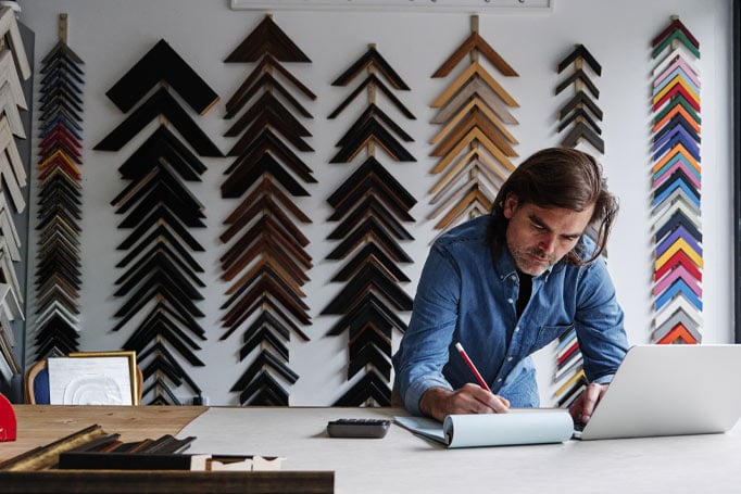 Man surrounded by pieces of wood, writing something down in a notebook