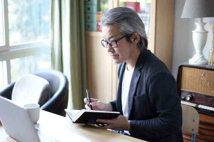 Man writing in a notebook while looking at laptop