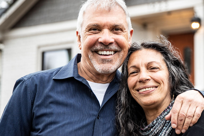 Older couple holding one another outside their home
