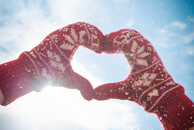 A person wearing mittens forming a heart with their hands