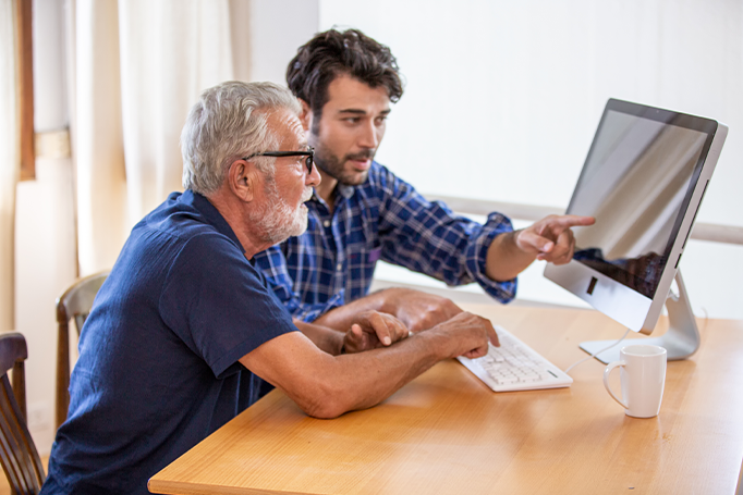younger man helping an older man with his computer