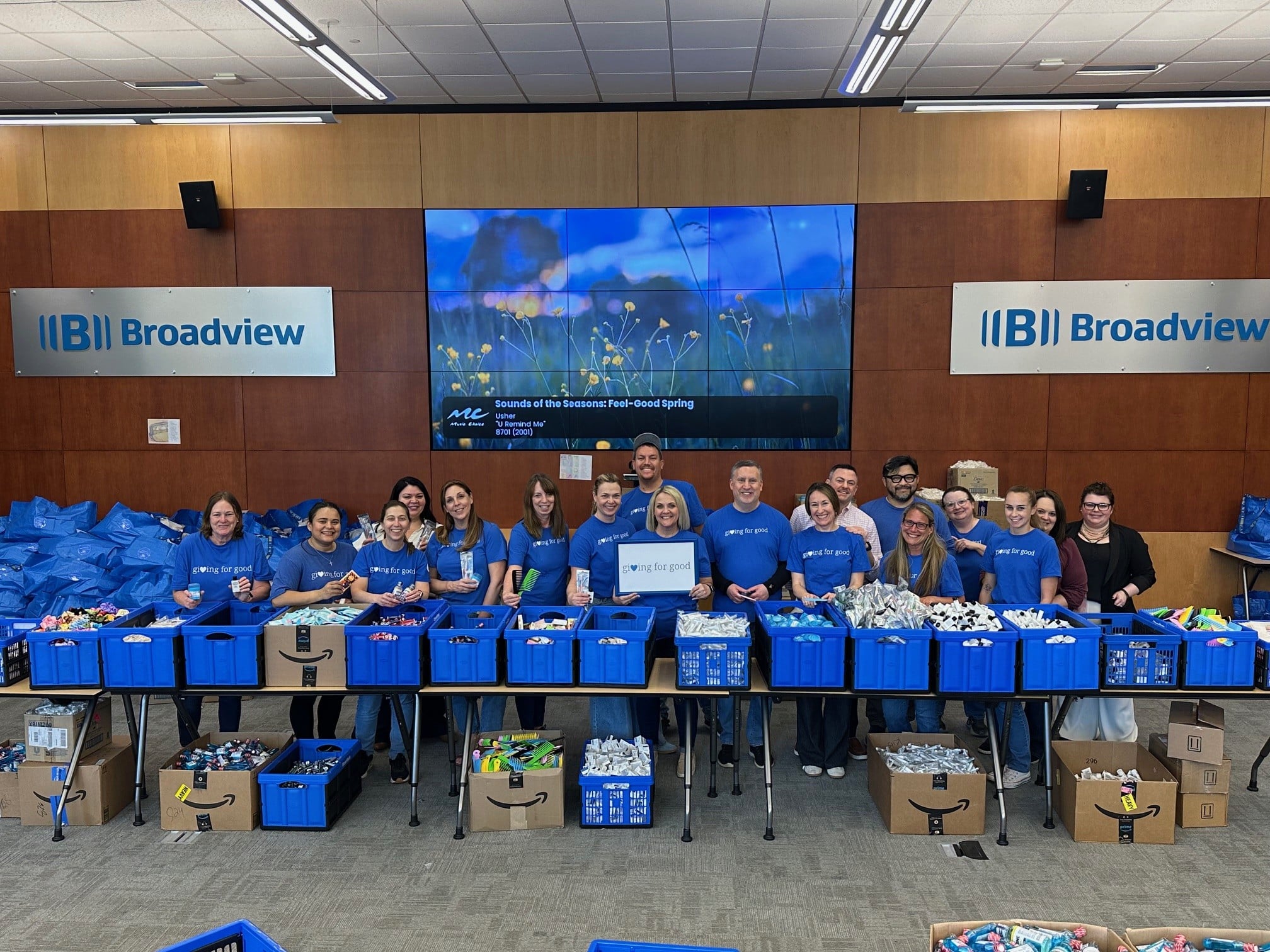 Broadview volunteers wearing Giving for Good shirts surrounded by items to make care kits.