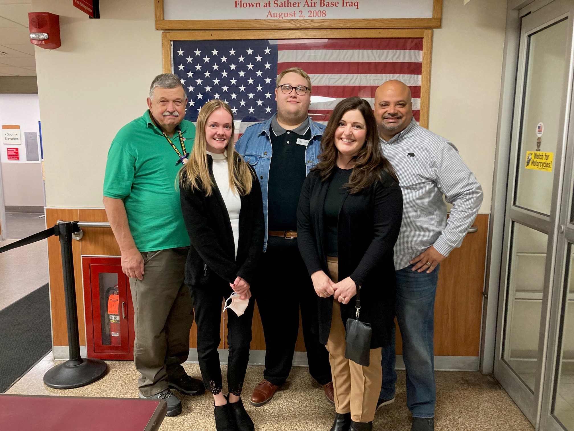 Group of five people standing in front of a framed American flag