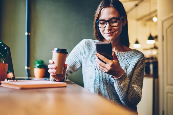 Woman holding her coffee cup and looking at her phone