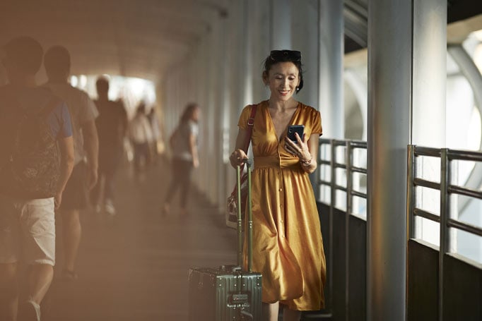 Woman walking through airport with her luggage and looking at her phone