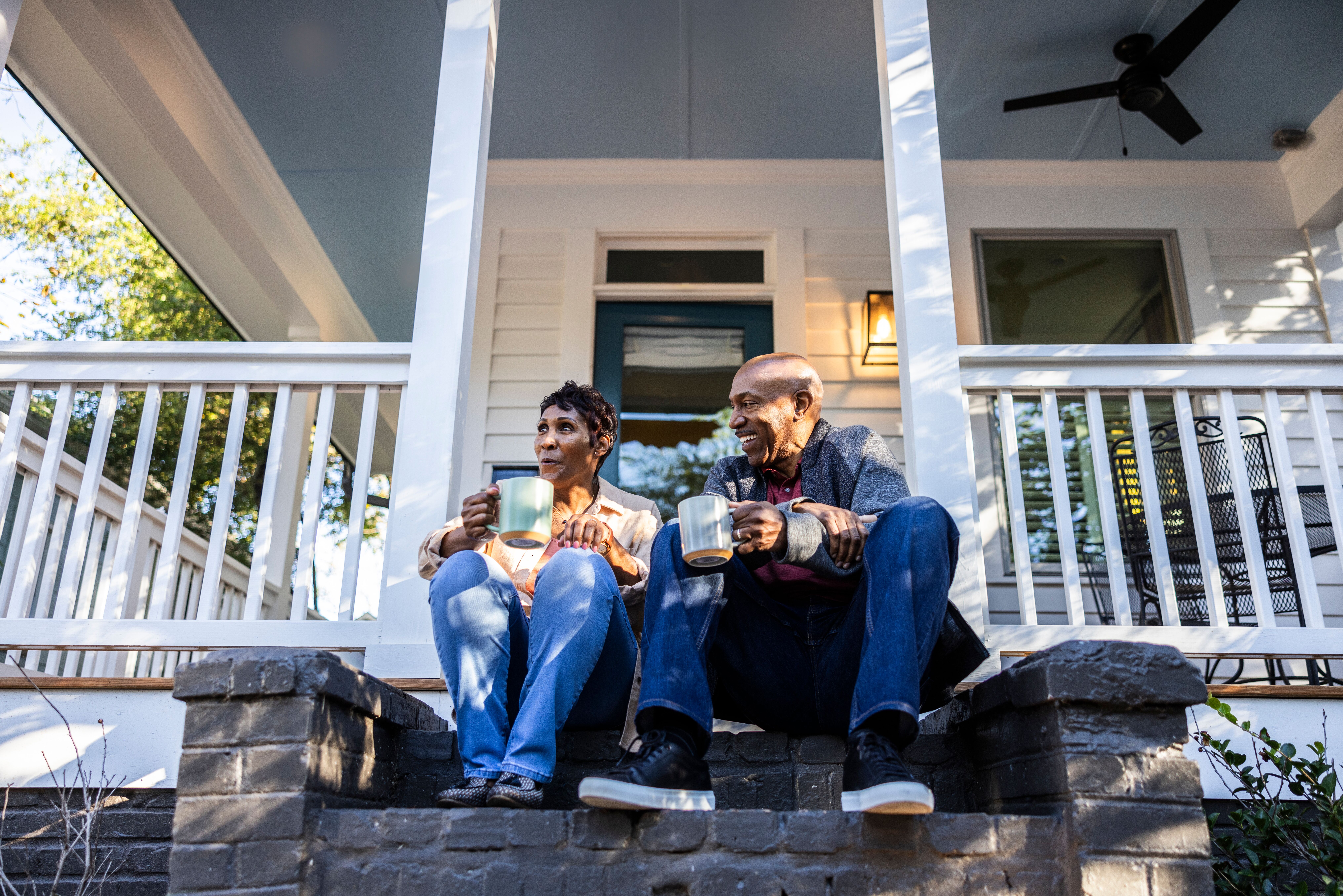 Couple sitting outside their house with coffee mugs.