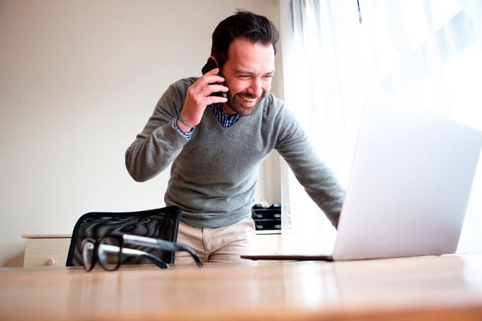 Man talking on the phone while looking at his laptop