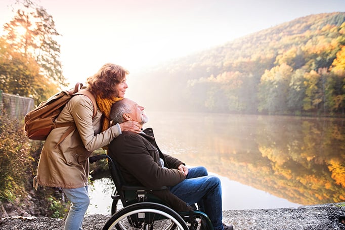 Woman has hands on the shoulders of a man in a wheelchair on a lake