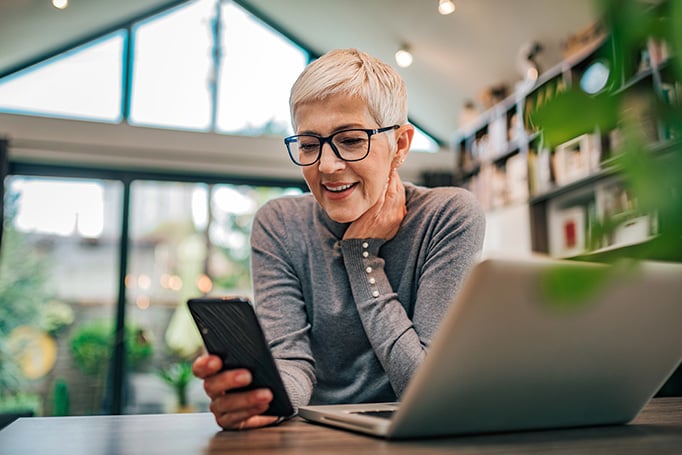 Woman looking a phone with her laptop 