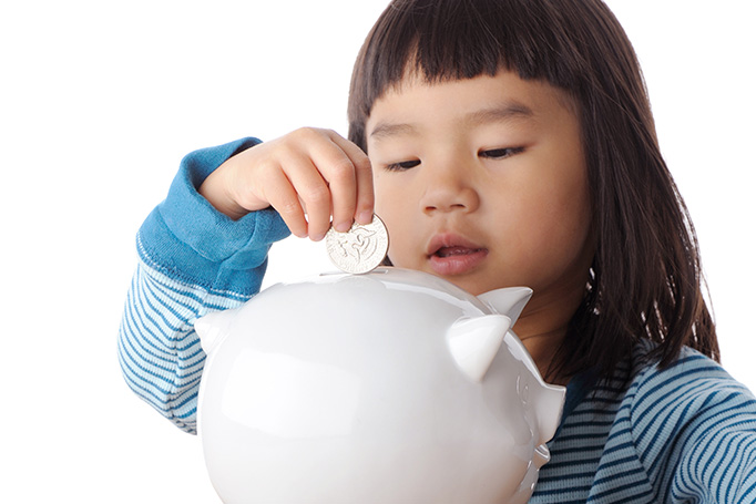 child putting coin in piggy bank