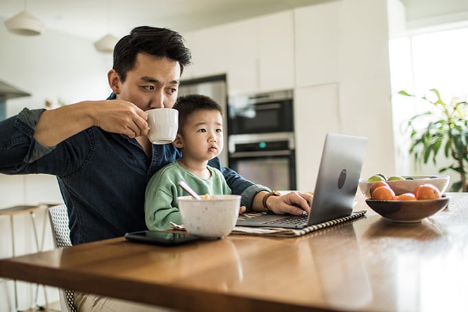 Son sitting on father's lap while he holds his cup and looking at laptop
