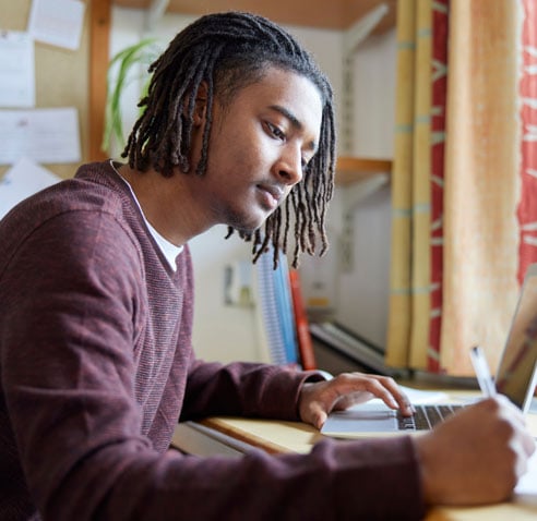 Student using his laptop and writing with a pen